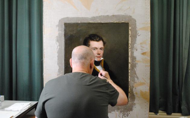 Een man is een schilderij aan het restaureren